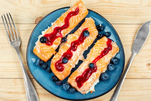 Roasted salmon fillet with blueberry berry sauce on ceramic plate.
