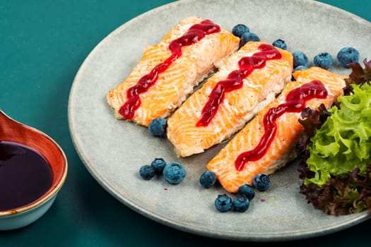 Roasted salmon fillet with blueberry berry sauce on ceramic plate.