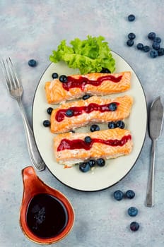 Roasted salmon fillet with blueberry berry sauce on ceramic plate.