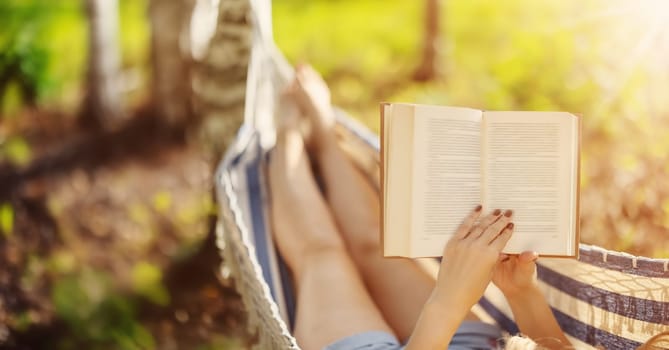 Woman lying in the hammock and reading an interesting book. Beautiful panoramic background.
