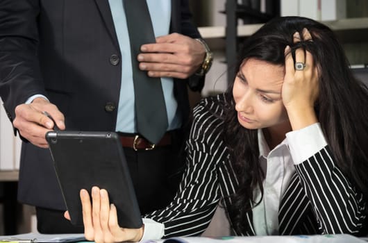 Unhappy businesswoman with tablet computer sitting on her office desk while discussion on business plan with businessman standing besides. Business concept.