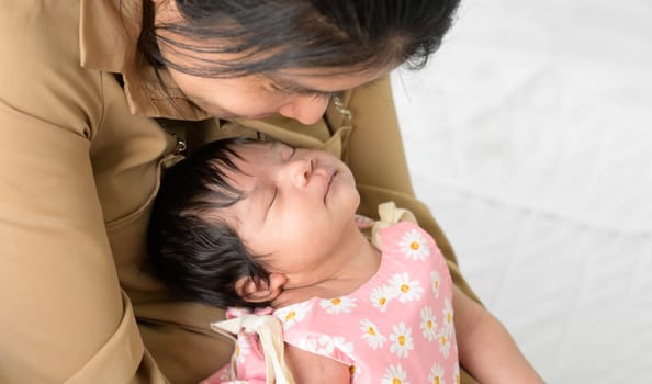 Happy newborn baby girl 1 month sleeping on mother arm. Mother sitting on whiet bed while nursing and looking her infant with love at home. Love, Health Care, love and mothers day concept