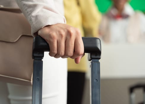 Close up of business woman hand holding handle of luggage at airport check in counter service
