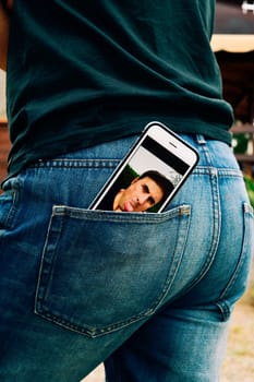 a smartphone with a picture of a young man sticking his tongue out in its screen, taken by myself, placed on the back pocket of the jeans of a young man