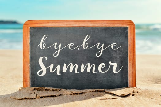 closeup of a chalkboard with the text bye, bye summer written in it, on the sand of a beach