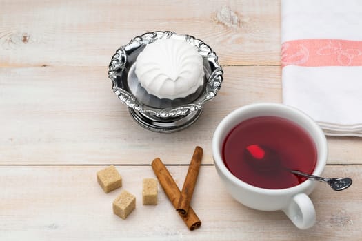 Cup of red tea. Cane sugar and cinnamon sticks with sweet dessert on wooden table