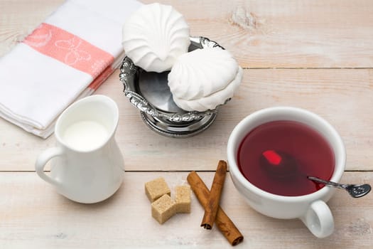 Black tea with milk. Cane sugar and cinnamon sticks with sweet dessert on wooden table