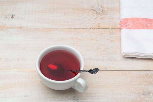 Cup of red tea with spoon on bright wooden background