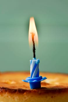 closeup of a cheesecake topped with a lit birthday candle against a rustic pale green wooden background