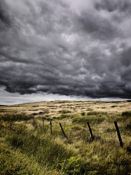 Intense looking clouds over a rural moorland. There is a poorly constructed fence running through the image.