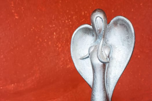 Upper body of a silver angel figure in front of terracotta colored wall