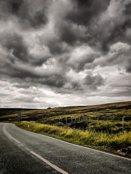 An asphalt road leading into an atmospheric moorland.