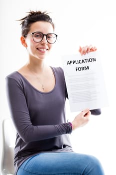 woman with glasses showing an application form and smiling sitting on a white office chair