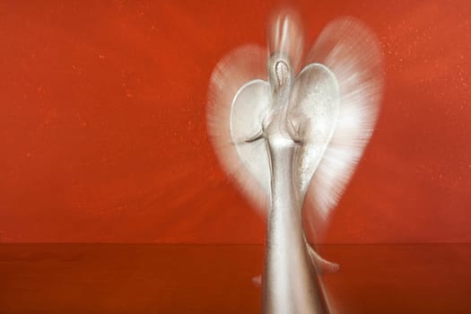 Upper body of a silver angel figure in front of terracotta colored wall with zoom effect