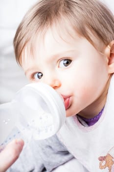 mother nursing her baby with a baby bottle while this little girl looks at the camera