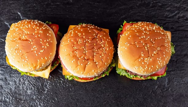 Low angle front view on three large chicken, beef and shrimp burgers stuffed with delicious toppings over wooden table