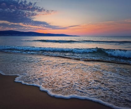 Dawn at the sea with foamy waves on the sand and colorful sky at the horizon. Sunny Beach coastline in Bulgaria. Summer and travel background