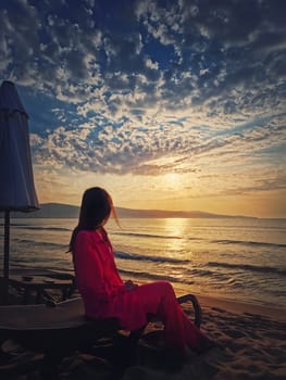 Woman relaxing on the sunbed as meets the dawn at the beach. Beautiful sea sunrise scene, summer vacation seaside, travel and holiday relaxation concept