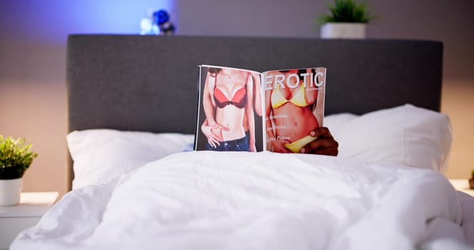 Man Lying On Bed Reading Erotic Magazine At Home