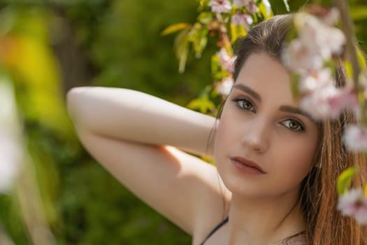 Cool brunette girl is posing on camera outdoors near sakura tree closeup.  Horizontally.