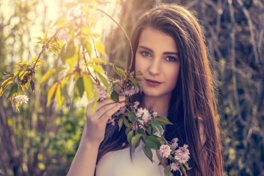 Attractive brunette girl posing on camera outdoors near sakura tree. Horizontally.