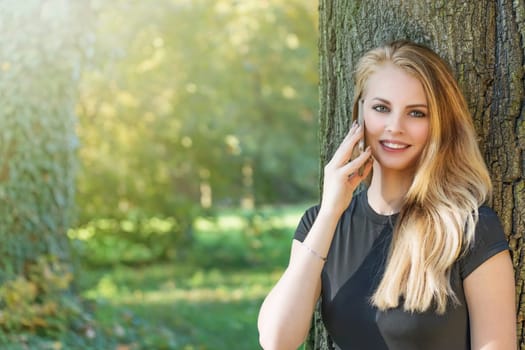 Attractive long haired young girl is on the phone outdoors . Horizontally.
