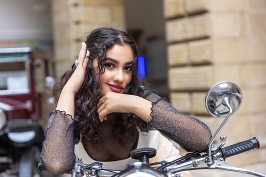 Portrait of  sexy tanned girl sitting on a vintage motorcycle with  hand in her hair.  Horizontally.