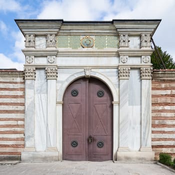 Decorated metal door with decorated white marble frame in stone brick wall at the First Courtyard of top Topkapi Palace, Istanbul, Turkey