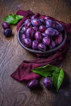 Fresh plums on plate over dark wooden background