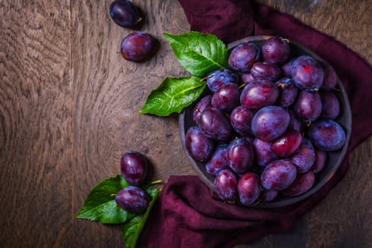Fresh plums on plate over dark wooden background