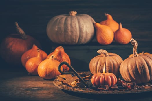 Autumn or fall harvest concept with pumpkins and candles on dark wooden background