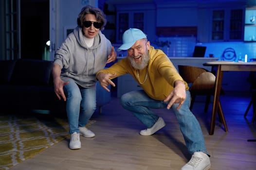 Funky senior couple wearing casual teen clothes posing in hip hop dance motion for camera