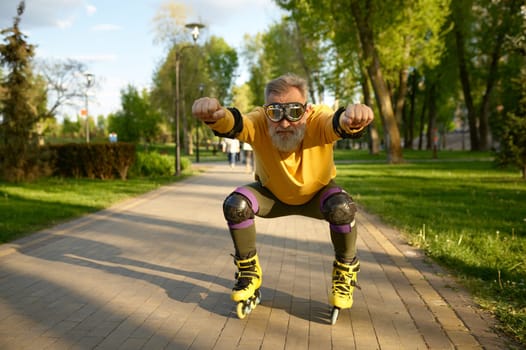 Senior man wearing funny goggles enjoying speed ride on roller skates over city park background at summer day