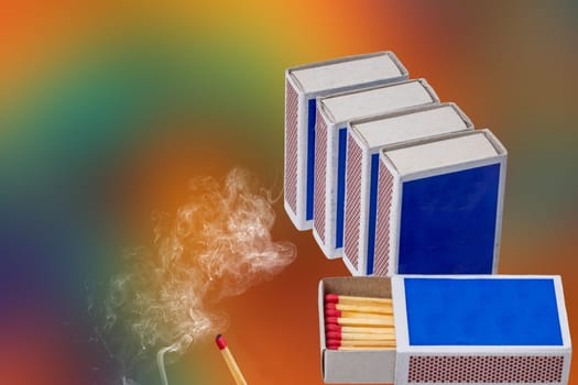 Matches, fire and smoke. Several matchboxes and rising smoke from a extinguished match against an abstract colorful background. Copy space.