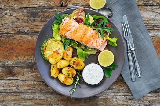Baked salmon fillet with potatoes and vegetables on wooden table in the garden summer time