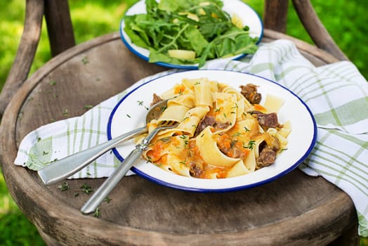 Pasta tagliatelle spaghetti with creamy sauce served on plate outside on sunny day. Eating fresh fettucine or pappardelle with meat in creamy sauce.