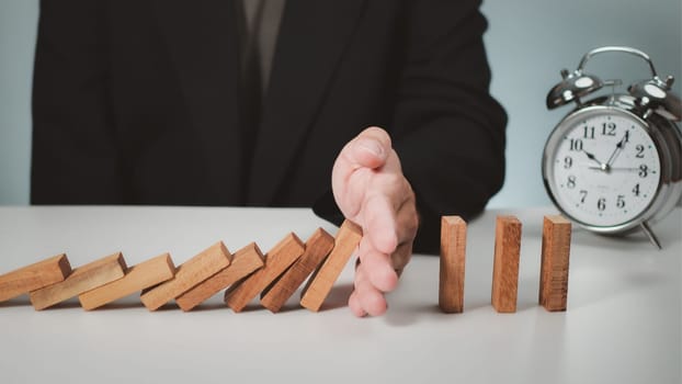 Risk management concept. Businessman hand stopping dominoes effect for business.