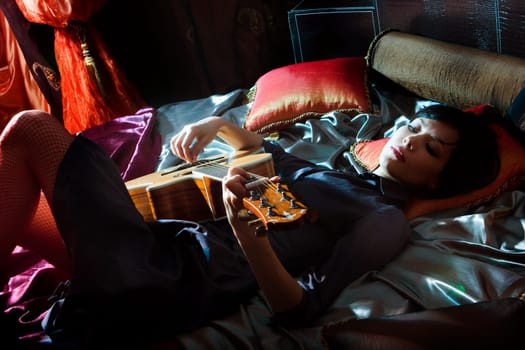 Young beautiful girl with acoustic guitar lying on the bed