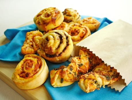 A selection of baked treats including tomato and herb sticks in a paper bag and baked scrolls.
