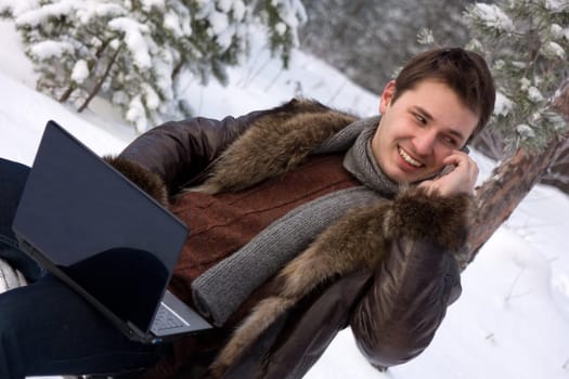 young man with laptop outdoors talking mobile phone