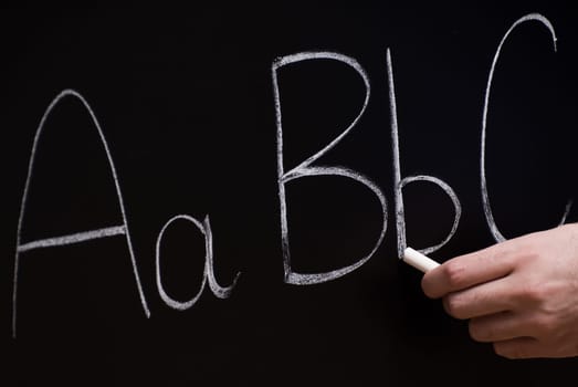 Closeup view of a teacher writing basic letters on the blackboard