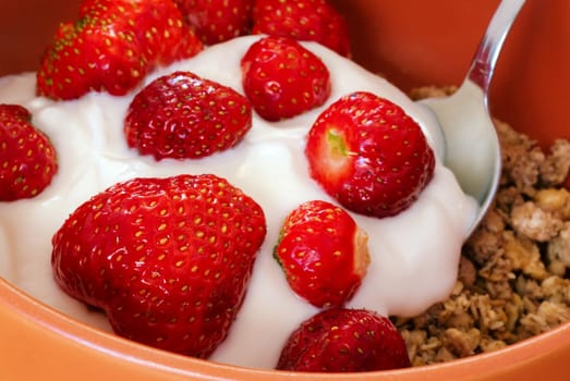 Detail of strawberry with yogurt and cereals and metal spoon in orange bowl