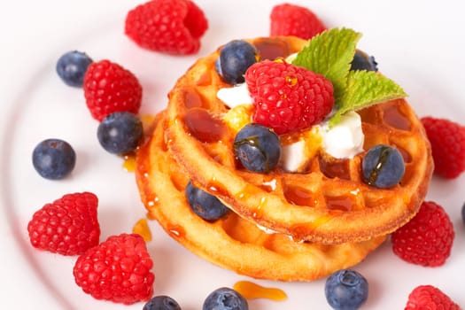 Belgian waffles with fresh strawberries, blueberries, mint leaves and cream on white plate