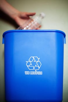 Woman's arm dropping plastic bottling into recycling container