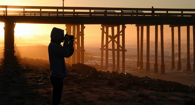 Photographer at sunset sunrise near the pier by the beach and ocean.