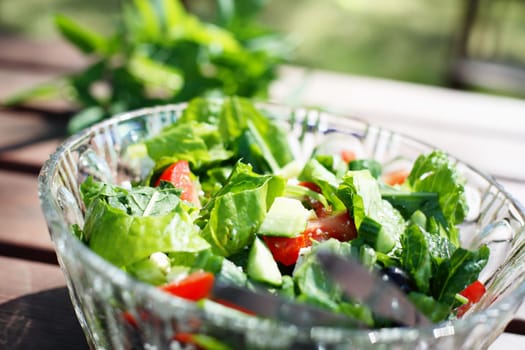 A close-up of a fresh garden salad on an outdoor wooden table.