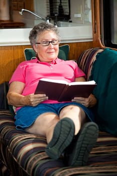 Senior woman reading a book in the living room of her motor home.