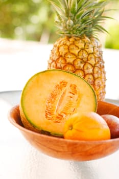 A colorful arrangement of tropical fruit on a glass table with a pineapple and rockmelon as the main items of focus.