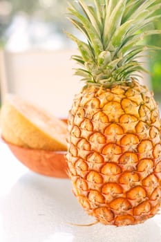 A colorful arrangement of tropical fruit on a glass table with a pineapple and rockmelon as the main items of focus.