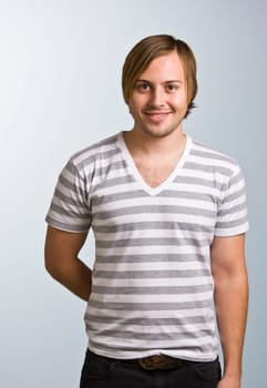 A young man wearing a striped shirt is smiling at the camera.  Vertically framed shot.